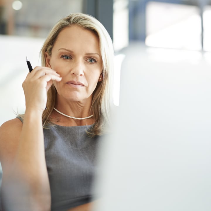 Female assisted living facility staff member sitting a working on a computer while holding a pen in one of her hands