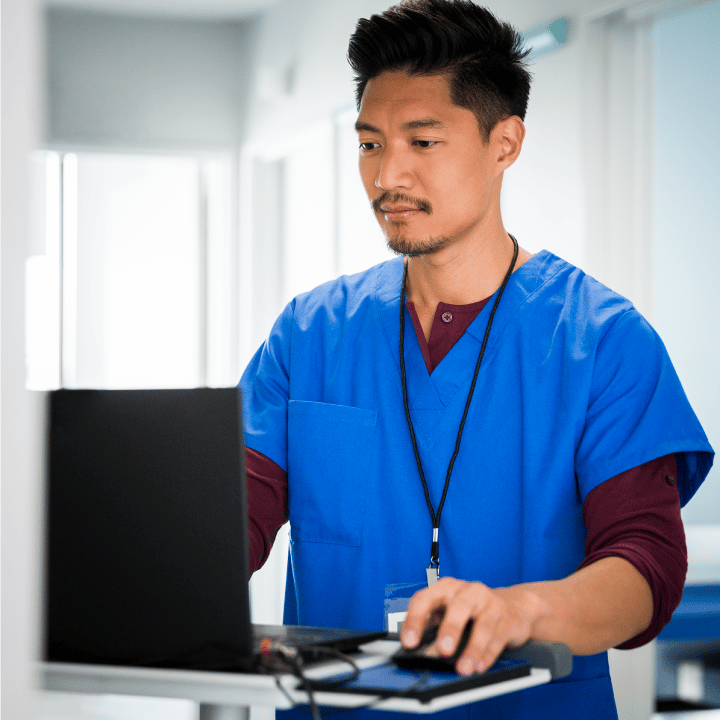 Male nurse in scrubs standing and using a laptop to review data on BPG clinical pathways