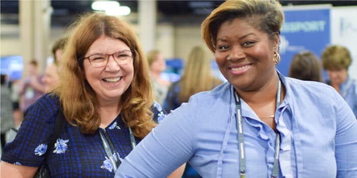 Two female user conference attendees smile while wearing badges
