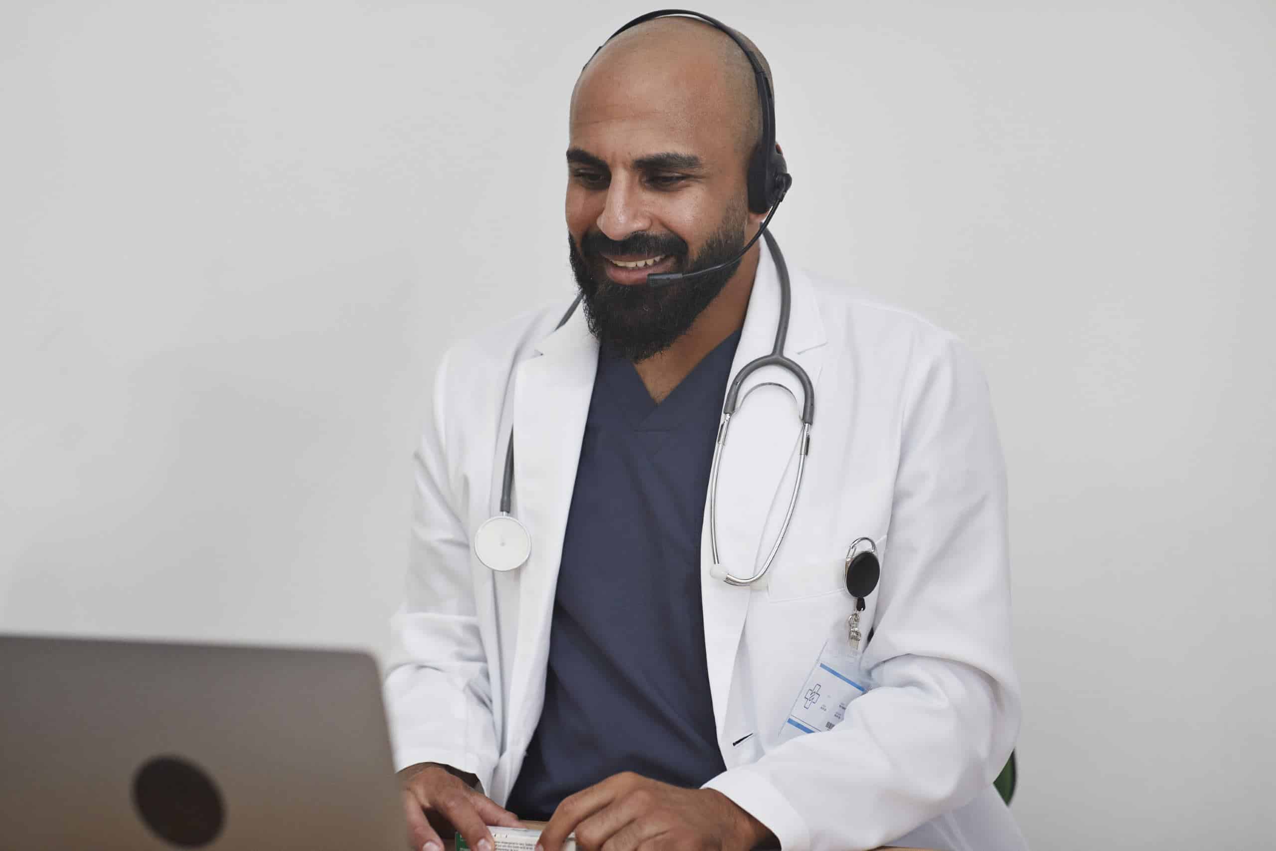 Male doctor in white coat confers with patient over video call on open computer
