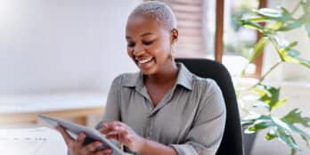 Female post-acute care facility executive sitting in her office smiling as she holds and uses a tablet device