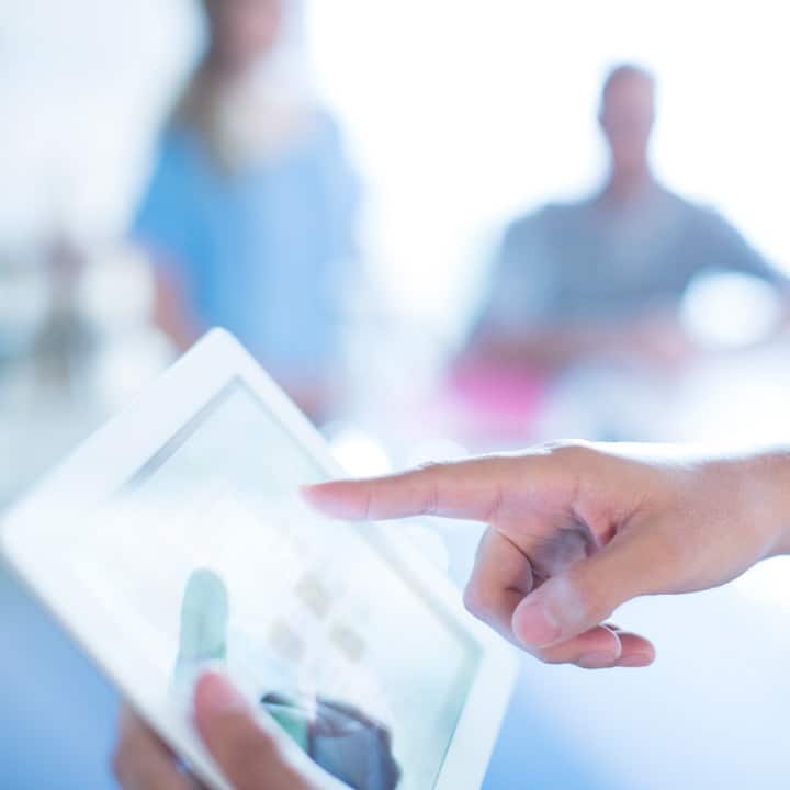 Close up of a hand holding a tablet device with the index finger of the other handing using the device