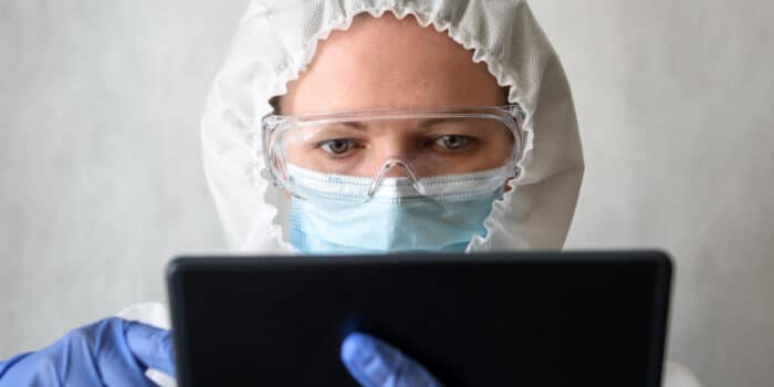 Close us up a female nurse's head as she's wearing full body protective equipment and using a tablet device