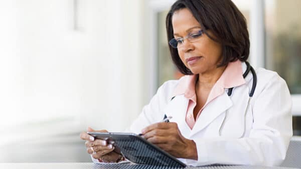 Female physician with a stethoscope around her neck standing and reviewing information on a tablet device