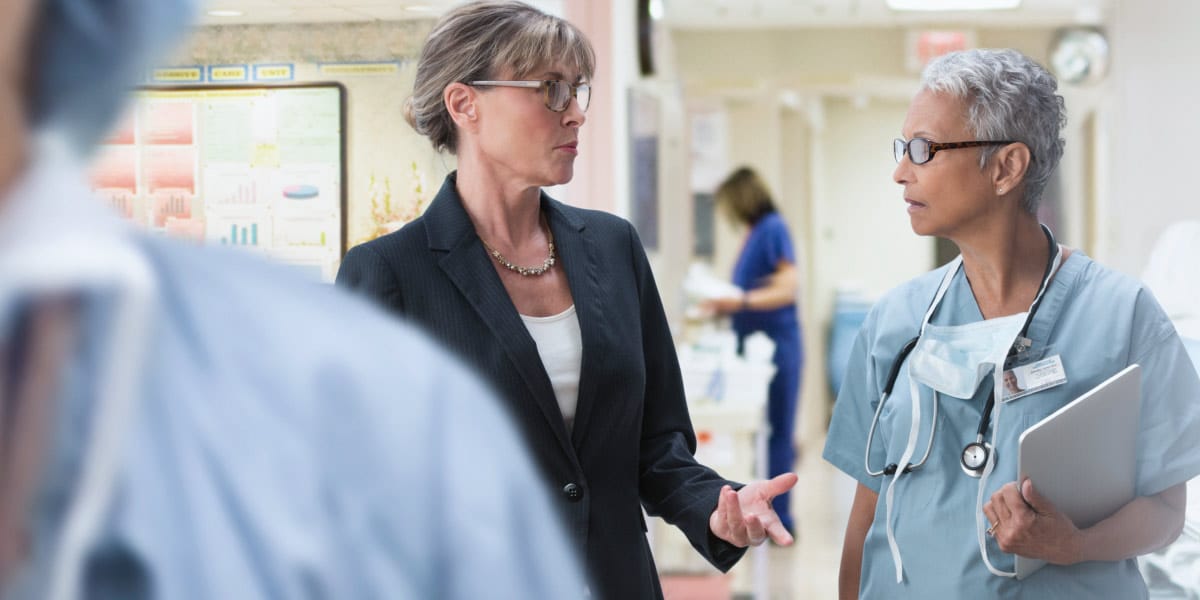 Female business professional standing and speaking with a female doctor in a hospital room