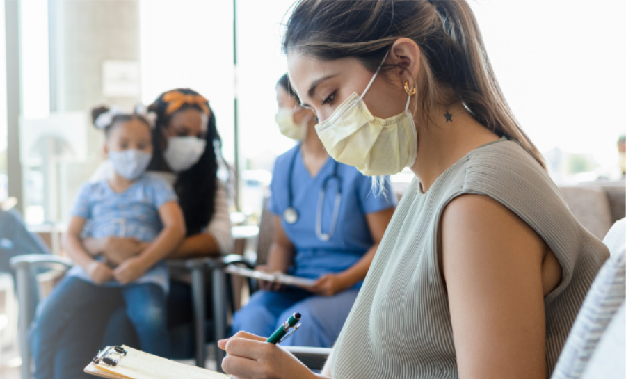 A young woman wearing a medical mask sits and writes on her clipboard