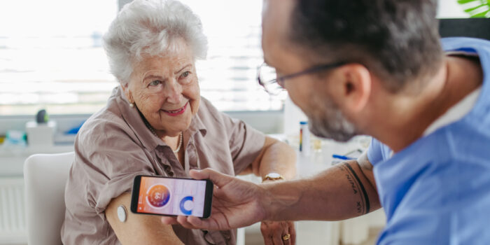 An elderly woman is having her glucose levels examined by a male nurse using an app on his phone